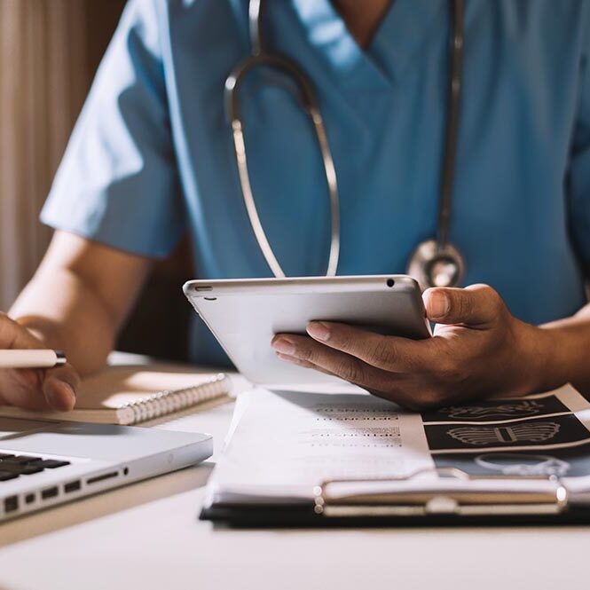 Doctor working on a tablet and laptop while viewing medical charts.